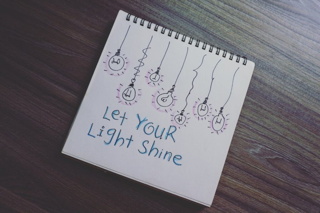 pexels-photo-1631487 A notebook with a motivational quote and light bulb drawings on a wooden table.